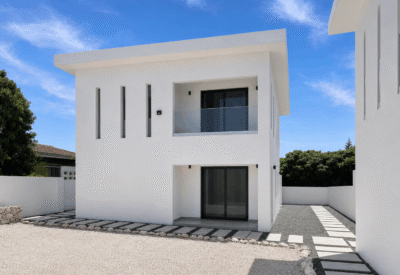 Moderne witte woning met groot terras en glazen deuren onder een blauwe hemel.