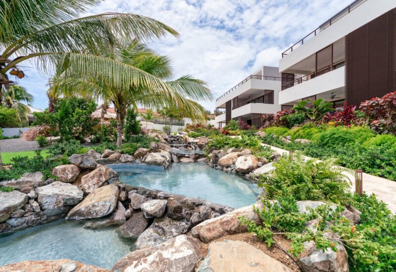 Luxe villa met tuin, zwembad en tropische planten in zonnige omgeving.