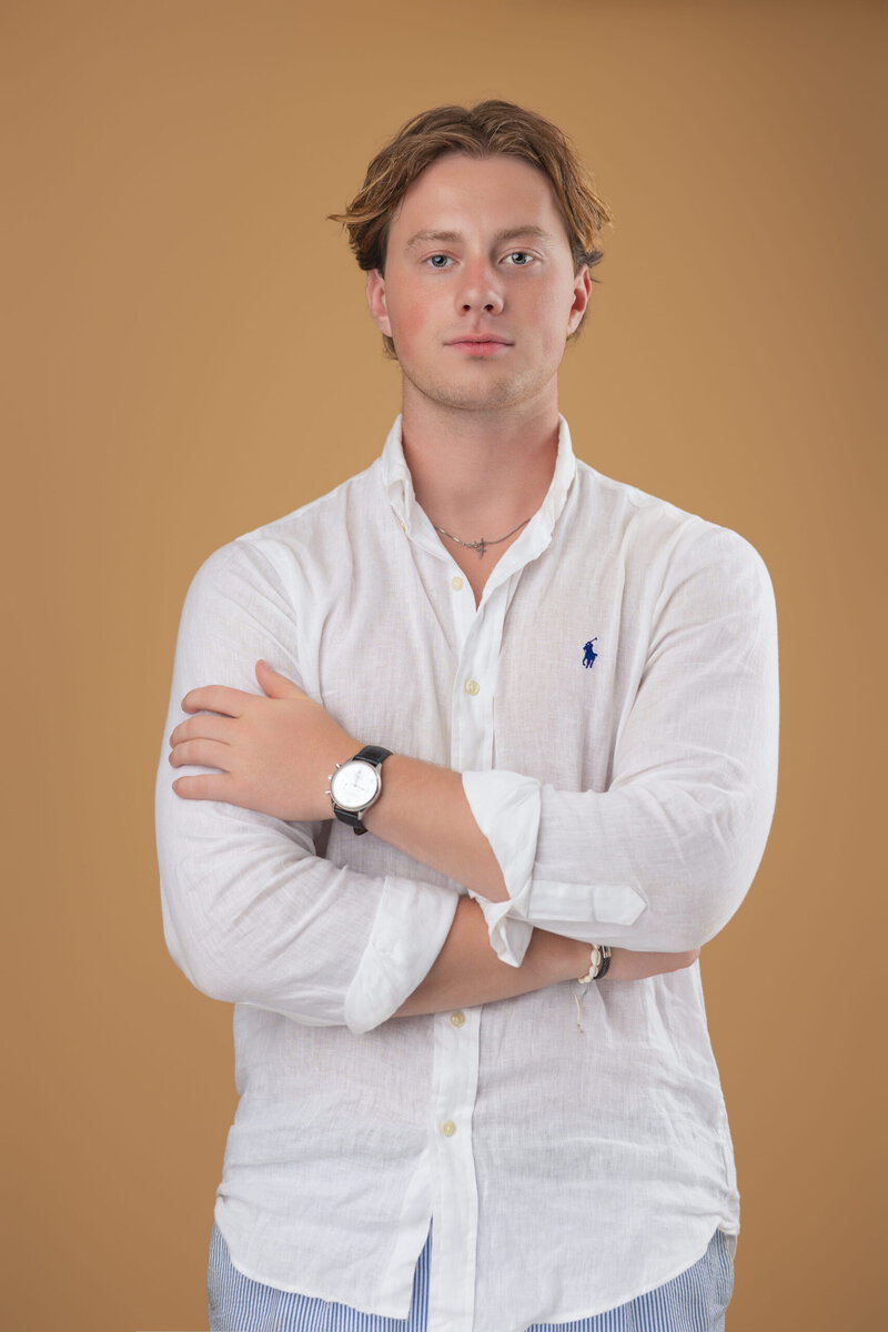 Jonge man in witte overhemd met armen over elkaar voor Sunset Realtors.