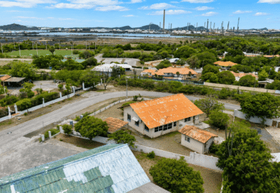 Landschap met huizen, bomen en industrie op de achtergrond.