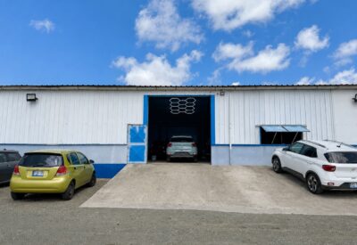 Bedrijfsloods met open deur en geparkeerde auto's voor de ingang.